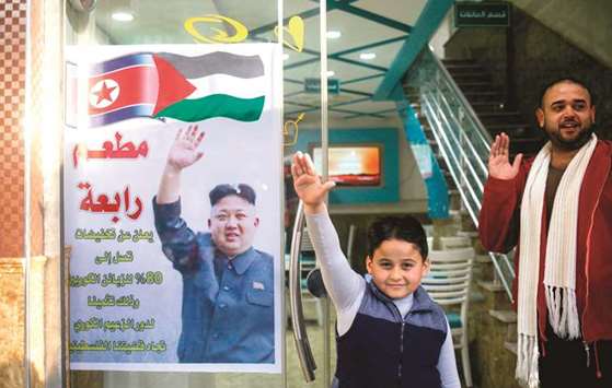 Salim Rabaa (right), the Palestinian owner of Rabaa restaurant and his son gesture with their right hands imitating a poster of North Korean leader Kim Jong-un, at the gate of the Jabalia refugee camp in the northern Gaza strip yesterday. The sign at the entrance of the restaurant reads in Arabic: u201cSpecial discounts reaching up to 80% for Korean patrons, in appraisal of the role of the Korean leader towards our Palestinian cause.u201d