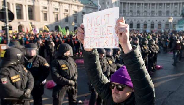 A protester stands in front of the riot policemen and holds a sign reading ,Not my Government, during a protest near presidential palace during the inauguration of the new Austrian government in Vienna