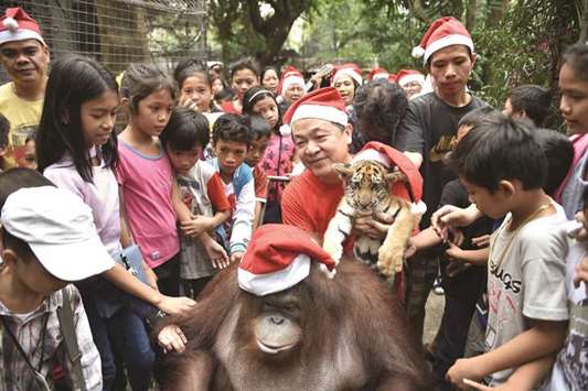 Zoo owner Manny Tangco (centre, in red shirt) sits next to an orangutan and a Bengal tiger cub during a party for orphanage children visiting a zoo in Malabon, suburban Manila, yesterday.