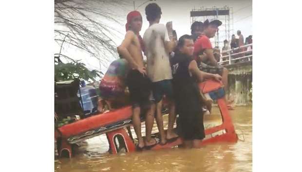 Residents stand stranded on a submerged vehicle during a flood in Cagayan de Oro, Mindanao, in this still image taken from a social media video obtained yesterday.