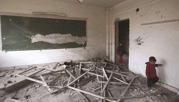 Syrian children walk in a heavily damaged classroom at a school turned into a shelter for people displaced by the war, in the rebel-controlled town of Hamouria, in the eastern Ghouta region on the outskirts of the capital Damascus.