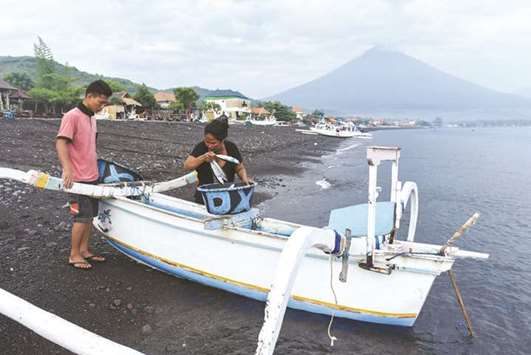 A woman collects fish from a fishing boat after it arrived on shore as Mount Agung is seen in the background from Amed, Karangasem, Bali, Indonesia.