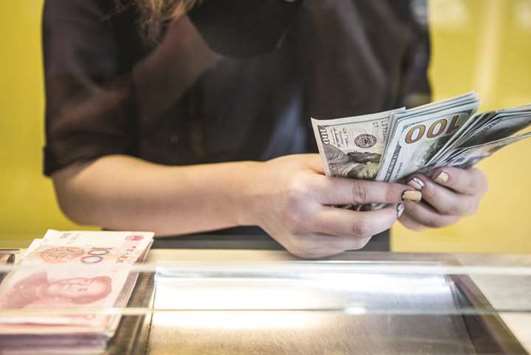 An employee at a currency exchange store counts US one-hundred dollar banknotes next to a pile of Chinese one-hundred yuan bills in Hong Kong (file). Chinau2019s reserves rose $10bn in November to $3.119tn, compared with an increase of $700mn in October, central bank data showed yesterday.