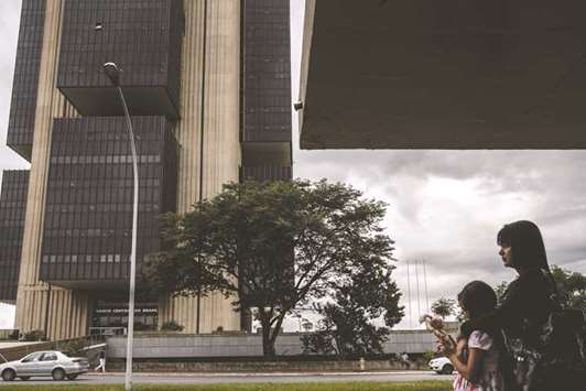 Pedestrians stand near the Central Bank of Brazil headquarters in Brasilia. Led by president Ilan Goldfajn, the banku2019s board lowered the Selic rate to 7% on Wednesday, following a previous 75 basis-point reduction in October.