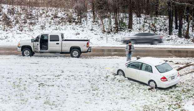 A motorist checks his phone after sliding off the road in the snow in North Carolina