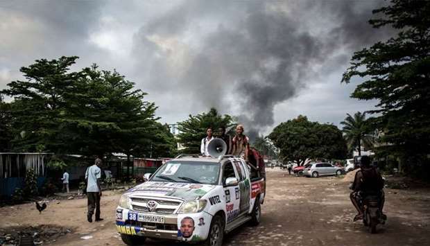 A campaign car is seen as smoke rises from a fire at the independent national electoral commission's (CENI) warehouse in Kinshasa