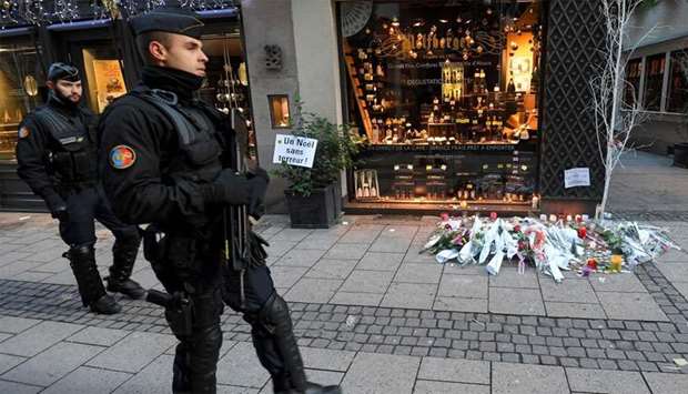 French gendarmes walk past flowers and candles laid in the street in tribute to the victims of a deadly shooting two days ago, in central Strasbourg