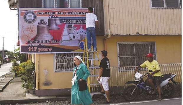 A Catholic nun walks past workers hanging a banner in Balangiga, in Eastern Samar province, yesterday, a day before a ceremony to return three bronze church bells taken by US troops in 1901.