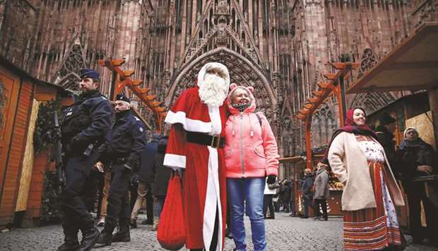 French police personnel keep watch outside the Strasbourg Cathedral while a man dressed as Father Christmas poses for a photograph with a tourist.