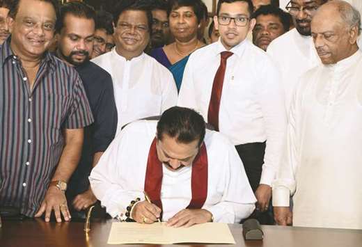 Mahinda Rajapakse, centre, signs a document backing down from his controversial appointment as prime minister in Colombo yesterday.