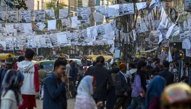 People walk under posters of election candidates hanging over a street during the general election campaign in Dhaka