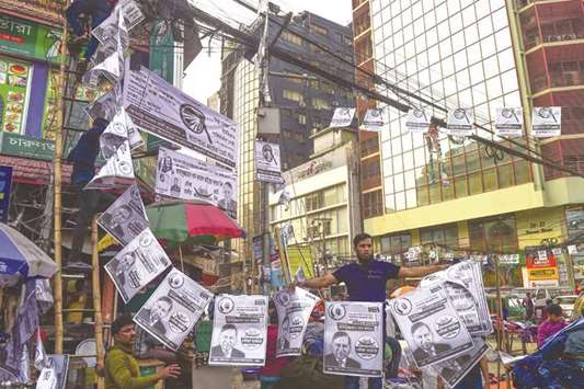 Bangladeshi ruling party supporters hang election camping posters in Dhaka yesterday.