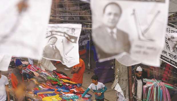 A Bangladeshi youth works in a shop as posters of election candidates hanging over a street during the general election campaign in Dhaka yesterday.