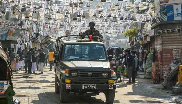Bangladeshi army personnel drive a military vehicle through a street adorned with election posters near a polling station in Dhaka