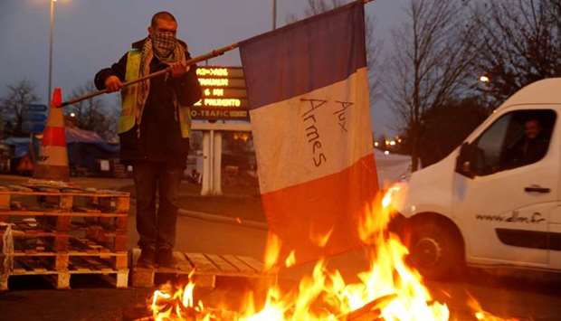 A protester wearing a yellow vest, the symbol of a French drivers' protest against higher diesel fuel prices, holds a flag near burning debris at the approach to the A2 Paris-Brussels Motorway, in Fontaine-Notre-Dame, France