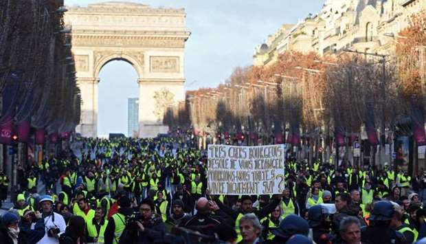 A ,yellow vest, (gilet jaune) protestor holds a sign reading ,Dear bourgeois we are deeply sorry to disturb you but could we all live with dignity please ?,
