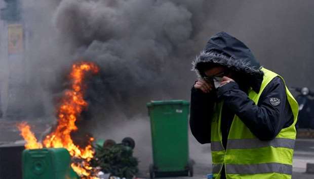 A protester wearing a yellow vest stands next to burning trash bins in a street during a national day of protest by the ,yellow vests, movement in Paris