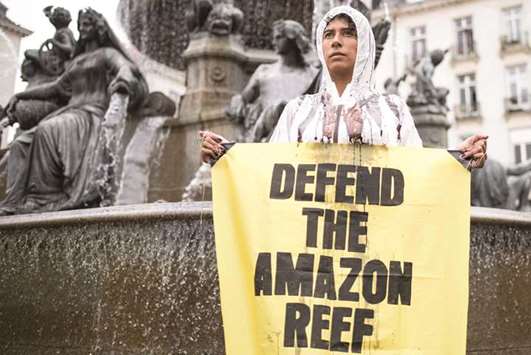 In this file photo taken on September 22, 2018 a Greenpeace activist stands in a fountain with a sign which reads u201c Defend the Amazon reef u201cduring a protest in Nantes, western France, against the drilling of oils wells by the French company Total in the Amazon Reef.