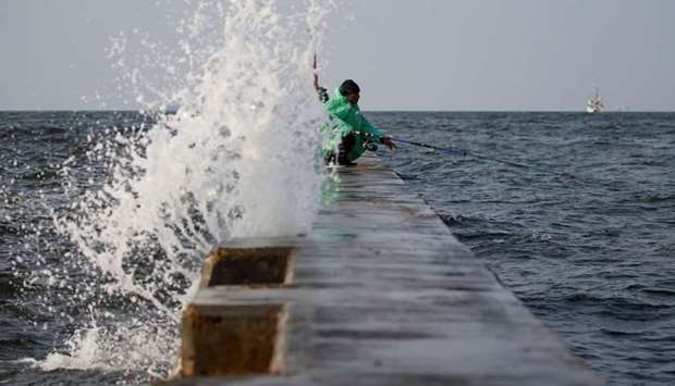 A man sits as he fishes at the sea wall built in an area affected by land subsidence and rising sea levels, during high tides in the northern coast of Jakarta, Indonesia