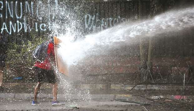 A demonstrator holds a makeshift shield to cover himself from a water cannon of the riot police during a protest against Chileu2019s government in Santiago, Chile.