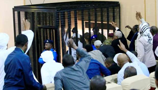 Sudanese former president Omar Hassan al-Bashir waves to supporters as he sits inside a cage during the hearing of the verdict that convicted him of corruption charges in a court in Khartoum, Sudan
