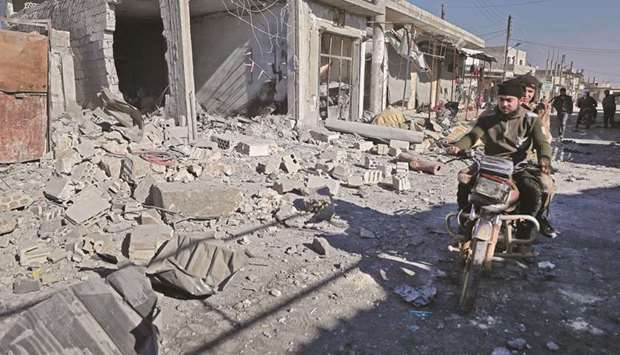 Syrians ride a motorcycle past debris at the site of a reported government bombardment in the village of Masaran on the outskirts of Maaret al-Numan in northwestern Idlib province, yesterday.