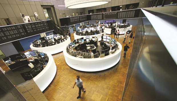 Traders work at their desks in front of the German share price index, the DAX board, at the Frankfurt Stock Exchange. The DAX 30 ended 2.1% lower at 12,964.68 points yesterday.