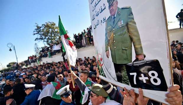 People hold up a portrait of Algeria's late military chief Lieutenant general Ahmed Gaid Salah as they gather outside the ,Palais du Peuple, (Palace of the People) during his funeral in Algiers