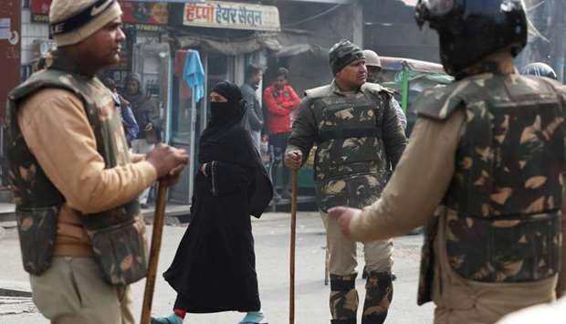 A veiled Muslim woman walks past policemen in riot gear on a street in Meerut, in the northern state of Uttar Pradesh, India
