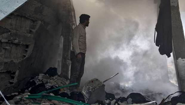 A man stands before a cloud of dust amidst rubble in a collapsed building following a reported air strike in the village of Balyun in Syria's northwestern Idlib province