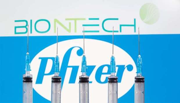 Syringes are seen in front of displayed Biontech and Pfizer logos