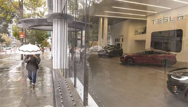 A pedestrian walks past a Tesla store in San Francisco. Some long-term investors say that they still expect to see Tesla post above-average gains due to increasing adoption rates in the global electric vehicle market and its solar energy business.