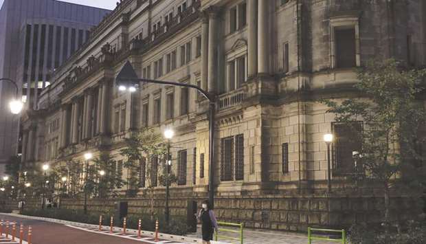 A pedestrian crosses a road in front of the Bank of Japan headquarters at dusk in Tokyo. Governor Haruhiko Kuroda conjured up another surprise at the BoJu2019s latest meeting, promising a review of its ultra-easy monetary policy without a total overhaul and leaving economists and investors with three months to speculate about possible changes.
