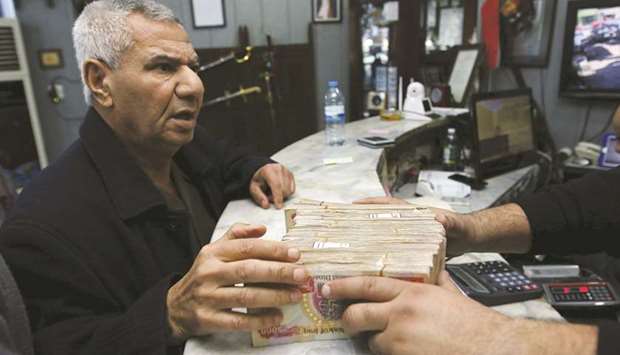 A man (left) changes Iraqi dinars to US dollars at a currency exchange shop in Baghdad (file). Iraqu2019s central bank has increased the sale price of US dollars to banks and currency exchanges to 1,460 dinars, from 1,182 dinars, seeking to compensate for a decline in oil revenue due to low crude prices, the bank said.
