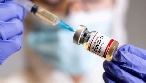 A woman holds a medical syringe and a small bottle labelled u2018Coronavirus Covid-19 Vaccineu2019