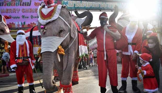 An elephant (centre L) from the Ayutthaya Elephant Palace, dressed in a Santa Claus costume and wearing a face mask, holds a basket containing face masks during an event outside the Jirasat Wittaya School in the central Thai province of Ayutthaya