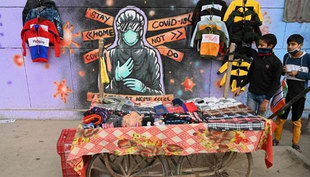 Boys walk past a roadside stall selling clothes in front of a mural representing a frontline warrior of the Covid-19 coronavirus, painted on a wall in New Delhi