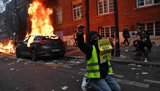 A ,Yellow Vest, (Gilet Jaune) anti-government protestor kneels raising his fist as he poses with a sign reading 'Living, Yes! Surviving, No!' near burning cars during a demonstration for 'social rights' and against the 'global security' draft law, which Article 24 would criminalise the publication of images of on-duty police officers with the intent of harming their 'physical or psychological integrity', in Paris