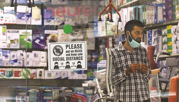 A man with a mask on his chin stands at the entrance of his shop for medical and fitness supplies displaying a precautionary sign for the customers as the outbreak of the coronavirus disease continues in Karachi. (Reuters)