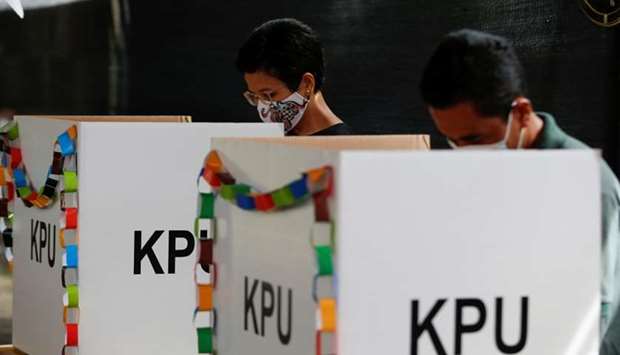 Voters wearing protective masks mark their ballots at a polling booth during regional elections in Tangerang, near Jakarta, Indonesia