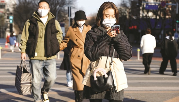 Pedestrians wearing face masks cross a street in Beijing on December 14. Economists said a current nationwide increase in Chinese coronavirus cases, and resulting  containment measures, appear to have led to cautious consumer behaviour just as a property market slump worsens.
