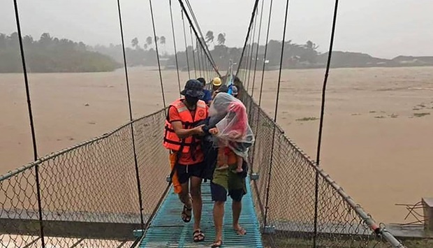 This handout photo taken and received on December 16, 2021 from the Philippine Coast Guard (PCG) shows a Coast Guard member accompanying evacuated residents as they cross a bridge over an overflowing river in Tubay town on southern Mindanao island, amid heavy rains brought about by Super Typhoon Rai.