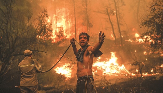 A local resident gestures as he holds an empty water hose during an attempt to extinguish forest fires approaching the village of Pefki on Evia (Euboea) island, Greeceu2019s second largest island, on August 8, 2021. (AFP)