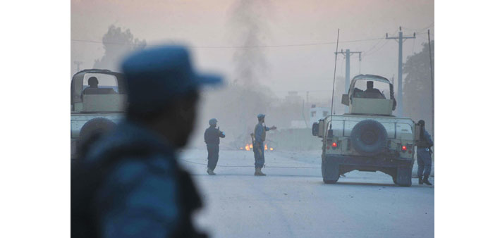 Afghan policemen keep watch as smoke billows in the background after an attack by Taliban militants on the Afghan intelligence service office in Jalal