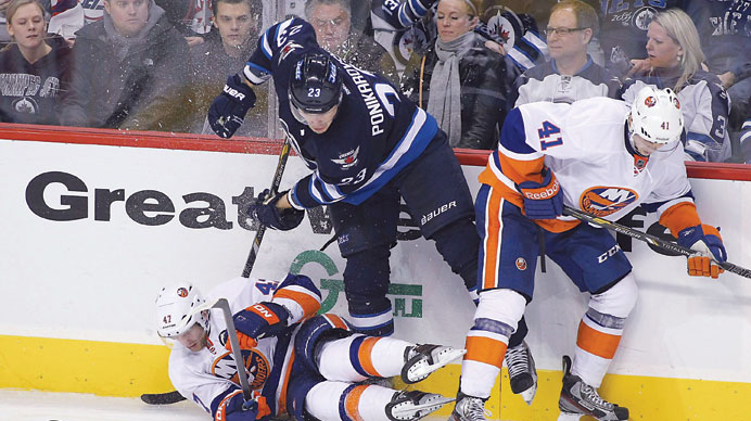 Andrew MacDonald and David Ullstrom of the New York Islanders collide with Alexei Ponikarovsky of the Winnipeg Jets against the boards in NHL action o