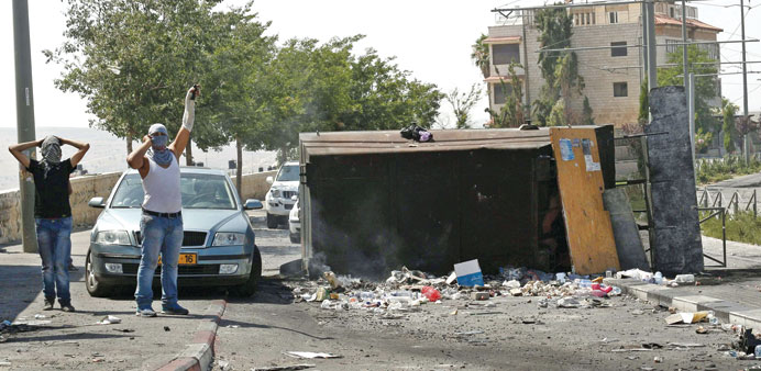Masked Palestinians stand beside an overturned container near the home of slain 16-year-old Mohamed Abu Khder in East Jerusalem yesterday.