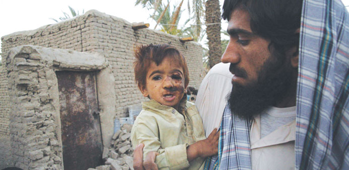 A survivor of an earthquake holds his daughter as he stands near his mud house after it collapsed following the quake in the town of Mashkeel, Baluchi