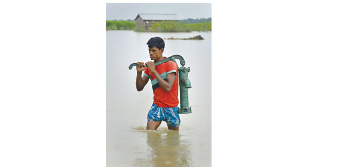 A man carries a water hand pump through flood waters Morigaon district of Assam yesterday.