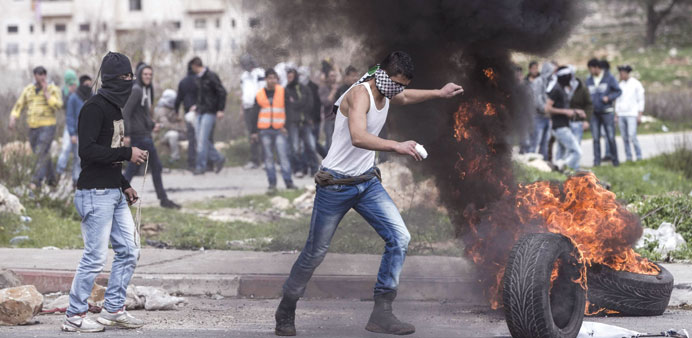 A masked man kicks a burning tyre during clashes next to the Israeli military prison u201cOferu201d in Beitunya, south of Ramallah, yesterday.