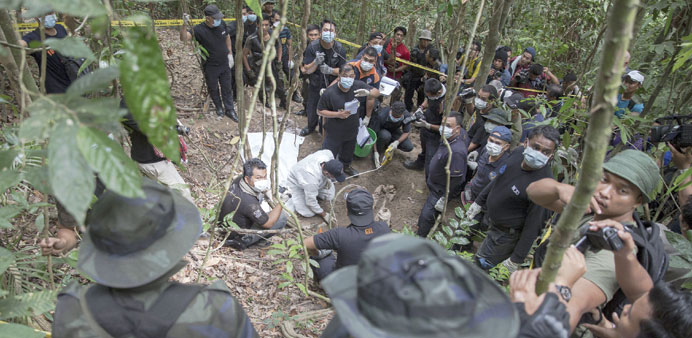 Policemen and reporters monitor as forensic experts dig out human remains near the abandoned human trafficking camp in the jungle close to the Thailan